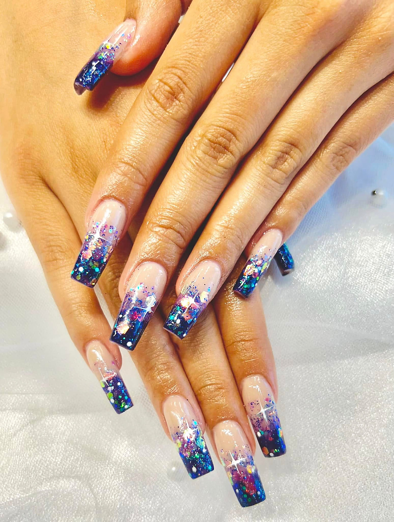 Long nails with galaxy glitter tips and hand-painted white stars on sheer white fabric